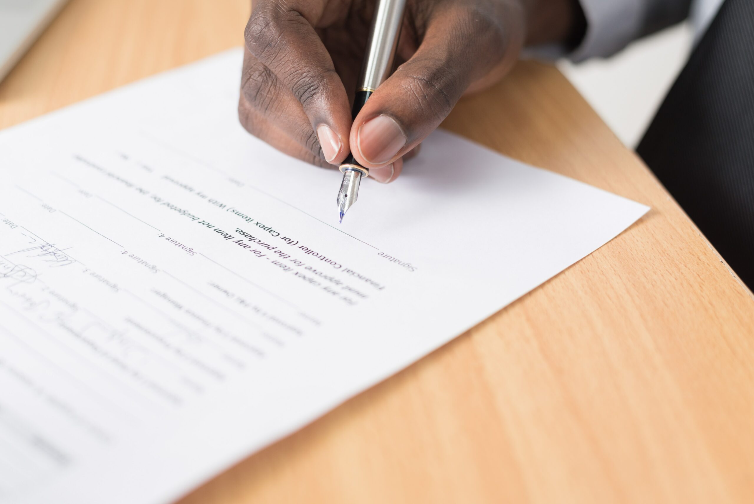 Human hand with a pen completing a type-written white paper.